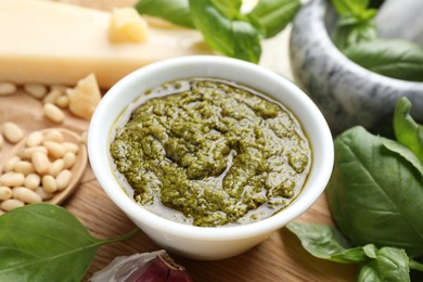 Photo of Tasty pesto sauce in bowl, basil, pine nuts and cheese on table, closeup