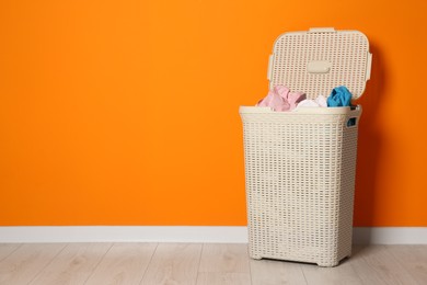 Open laundry basket with clothes near orange wall indoors, space for text
