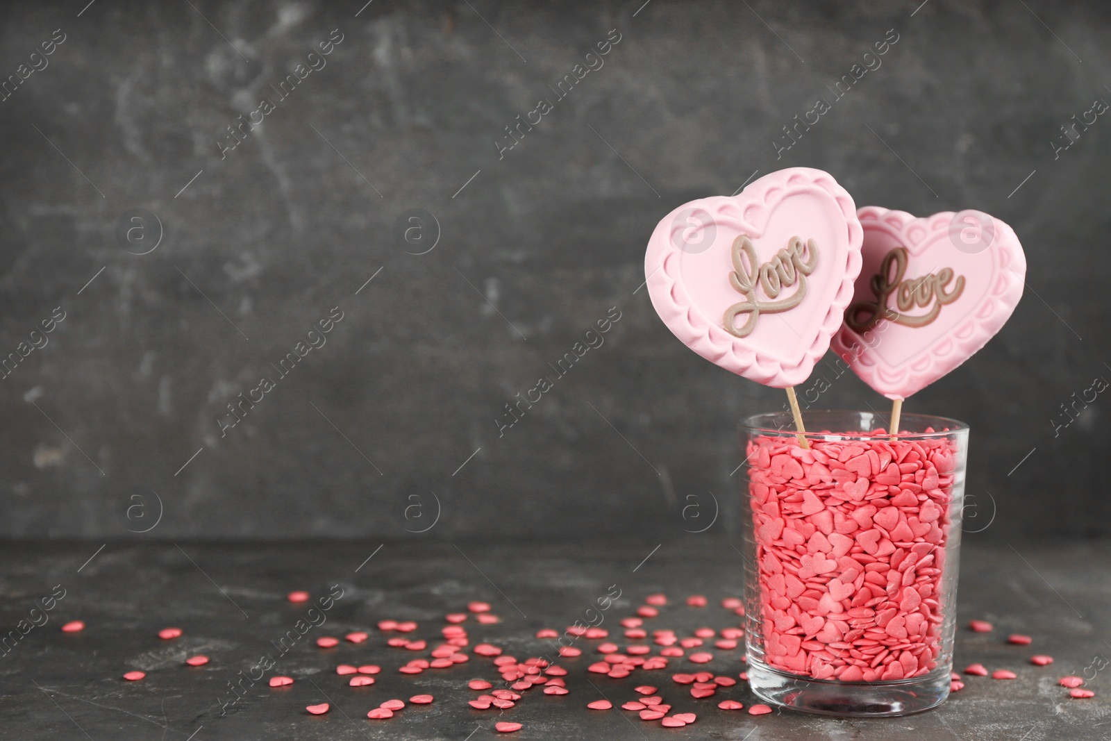 Photo of Heart shaped lollipops made of chocolate with sprinkles in glass on grey background, space for text
