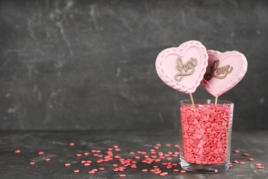 Heart shaped lollipops made of chocolate with sprinkles in glass on grey background, space for text