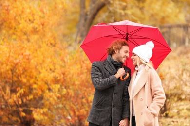 Photo of Young romantic couple with umbrella in park on autumn day