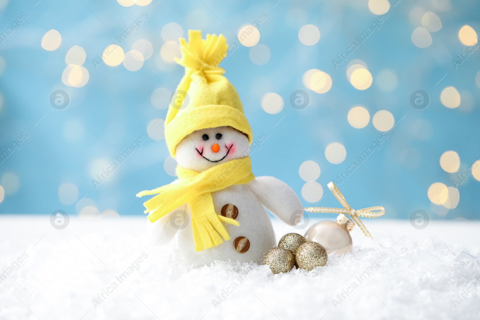Photo of Snowman toy and Christmas balls on snow against blurred festive lights, closeup