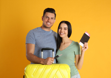 Happy couple with suitcase and tickets in passports for summer trip on yellow background. Vacation travel