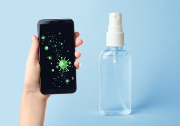 Image of Sanitizing mobile devices during coronavirus outbreak. Antiseptic spray and woman with smartphone on blue background, closeup