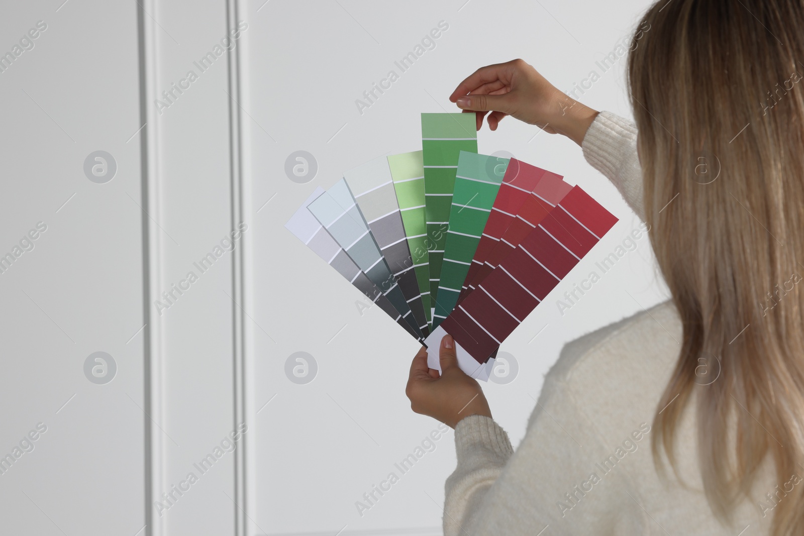 Photo of Woman choosing color for wall indoors, focus on hands with paint chips. Interior design