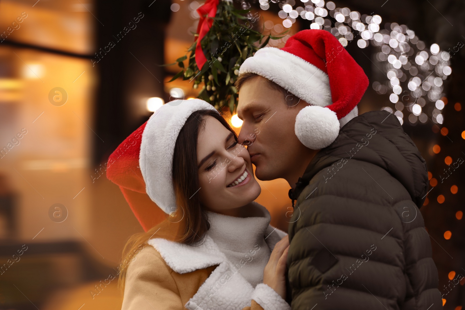 Photo of Happy man kissing his girlfriend under mistletoe bunch outdoors