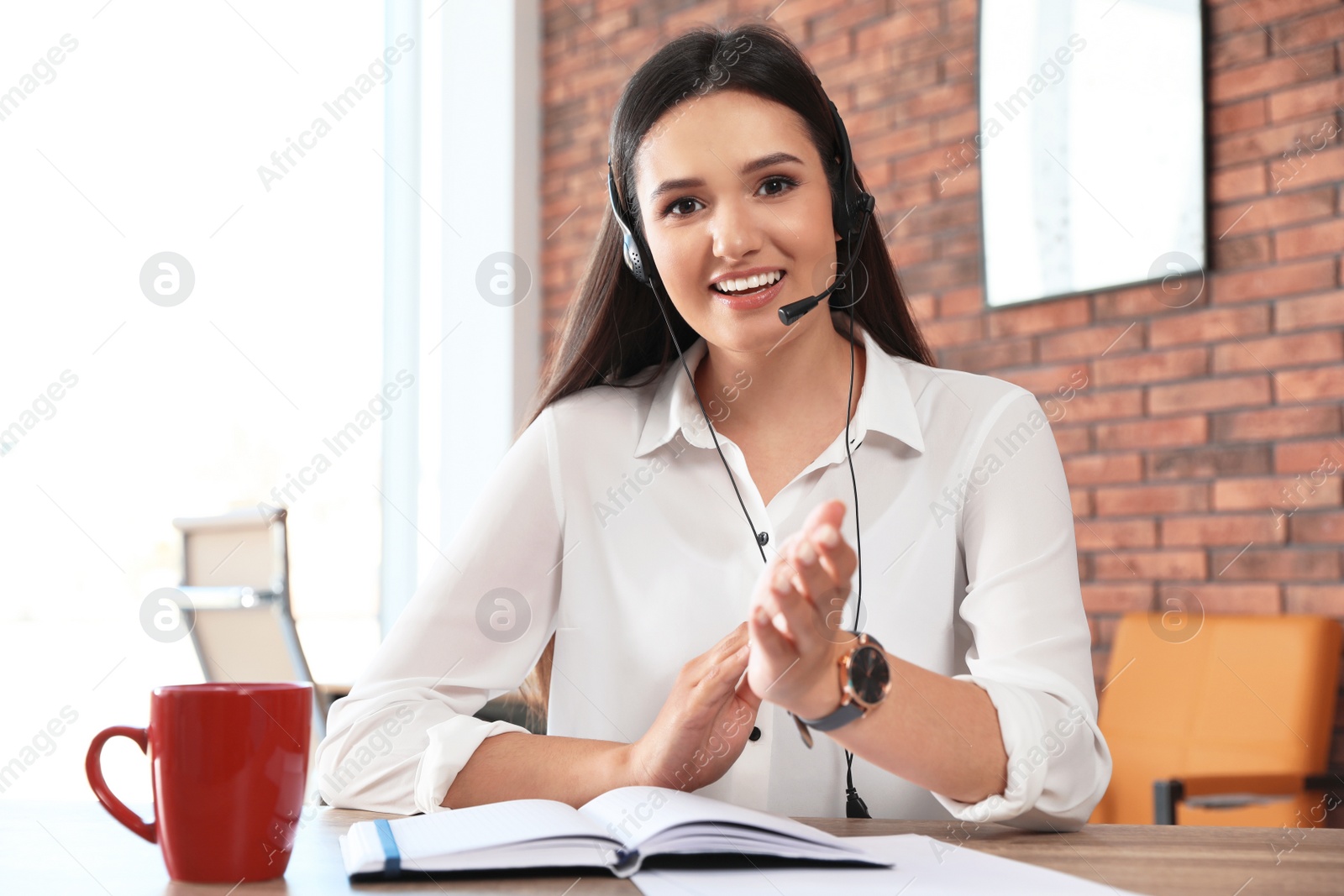 Photo of Young woman with headset looking at camera and using video chat in home office