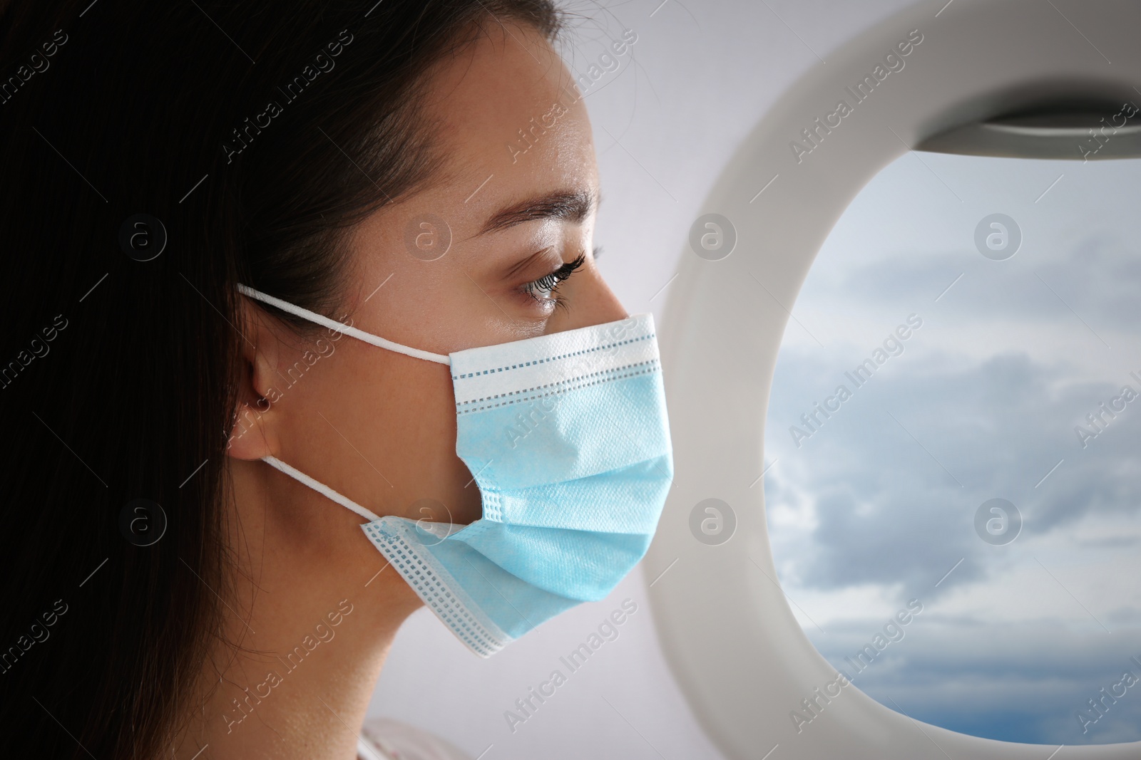 Image of Traveling by airplane during coronavirus pandemic. Woman with face mask near porthole