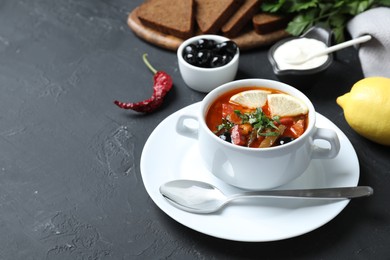 Photo of Meat solyanka soup with sausages, olives and vegetables served on dark grey textured table, space for text