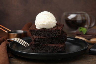 Photo of Tasty brownies served with ice cream on wooden table, closeup
