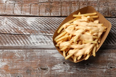 Delicious French fries with cheese sauce on wooden rustic table, top view. Space for text