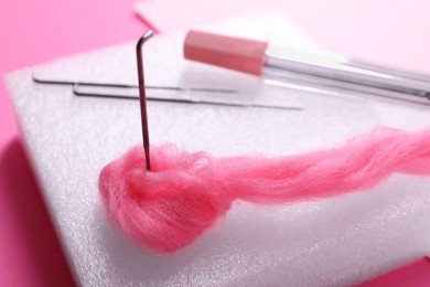 Felting mat, needles and wool on pink background, closeup