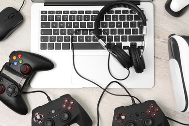 Photo of Gamepads, mouse, headphones and laptop on table
