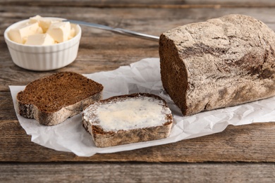 Photo of Slice of rye bread with butter near loaf on wooden table