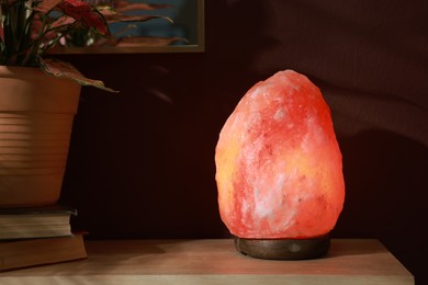 Photo of Himalayan salt lamp on wooden table near brown wall indoors