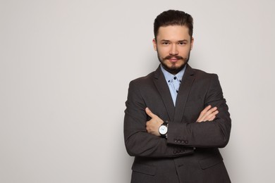 Handsome man in suit crossing his arms on light grey background. Space for text