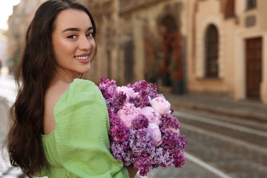 Photo of Beautiful woman with bouquet of spring flowers on city street, space for text