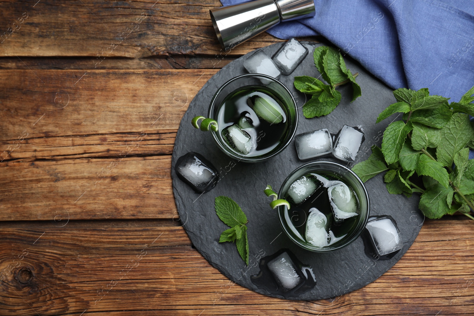 Photo of Delicious mint liqueur with ice cubes and green leaves on wooden table, flat lay. Space for text