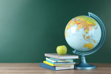 Photo of Globe, books and apple on wooden table near green chalkboard, space for text. Geography lesson