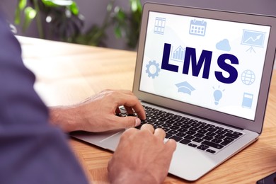 Learning management system. Man using modern laptop at wooden table, closeup. Different icons and abbreviation LMS on screen