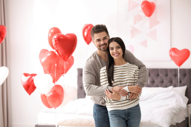 Photo of Lovely young couple in bedroom decorated with heart shaped balloons. Valentine's day celebration