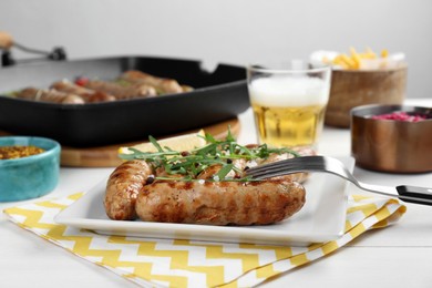 Photo of Tasty grilled sausages served with arugula and beer on white wooden table, closeup