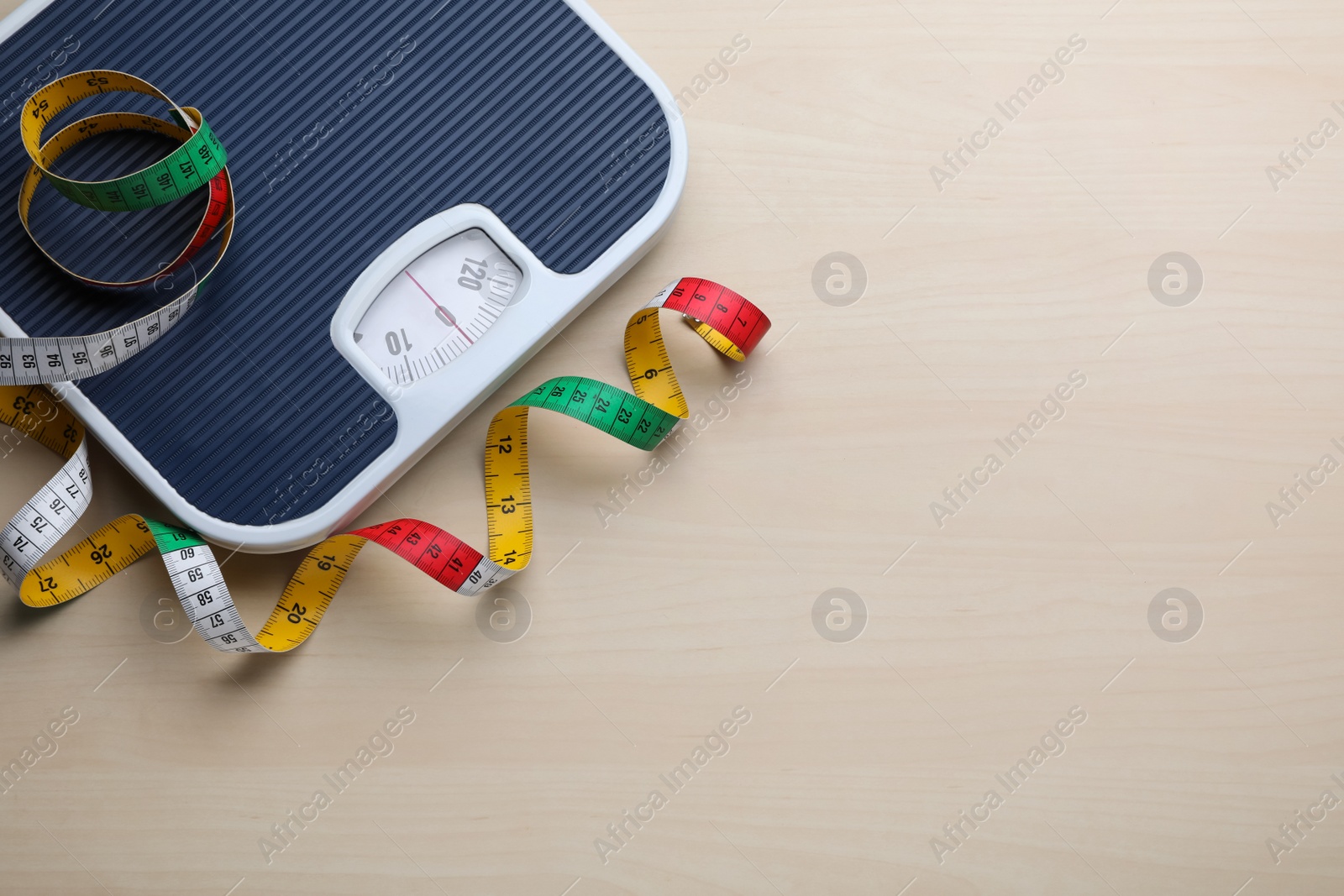 Photo of Bathroom scale, measuring tape and space for text on wooden floor, top view. Weight loss concept