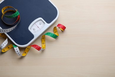 Bathroom scale, measuring tape and space for text on wooden floor, top view. Weight loss concept