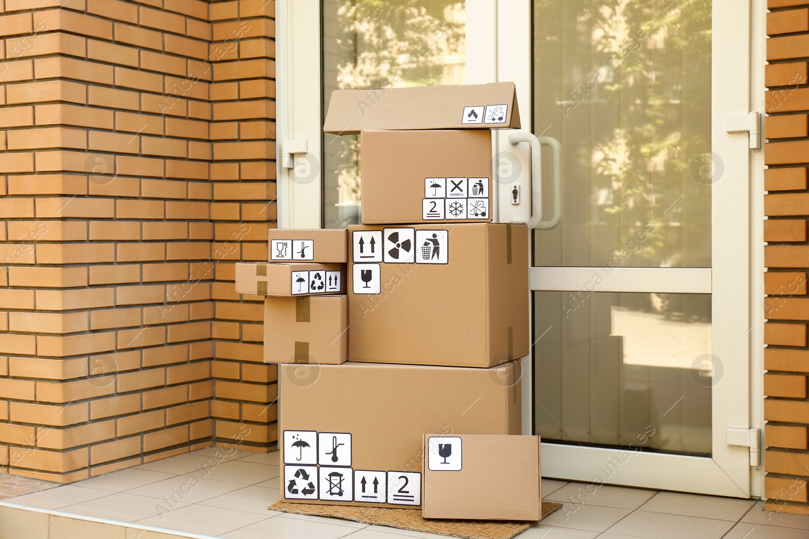 Photo of Cardboard boxes with different packaging symbols on door mat near entrance. Parcel delivery