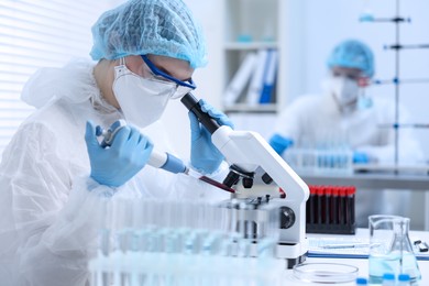 Scientist dripping sample onto glass slide while working with microscope in laboratory