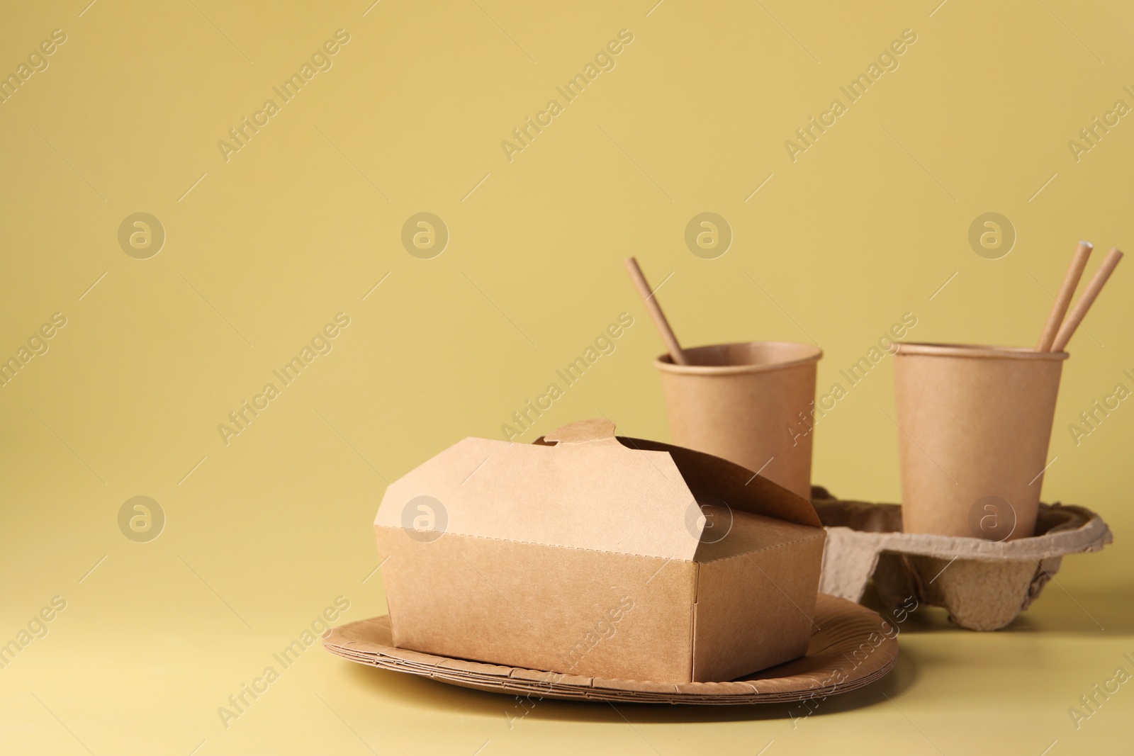 Photo of Eco friendly food packaging. Paper containers, cardboard cup holder and straws on pale yellow background, space for text