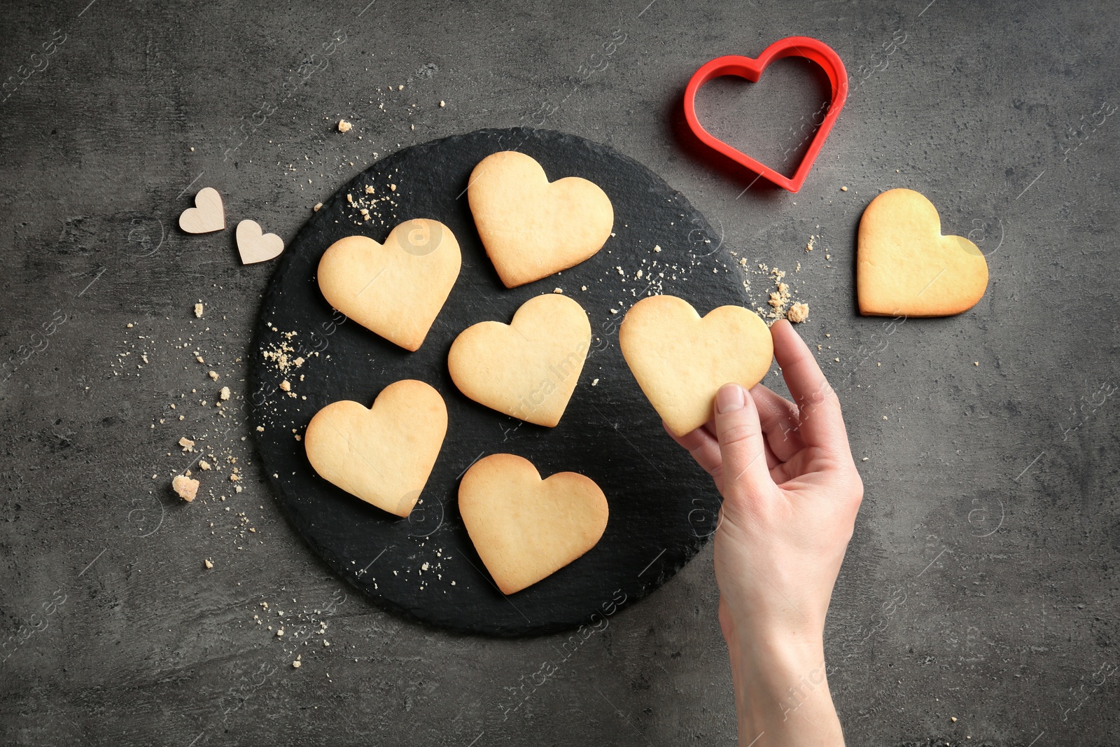 Photo of Woman holding homemade heart shaped cookie over table with pastry, top view