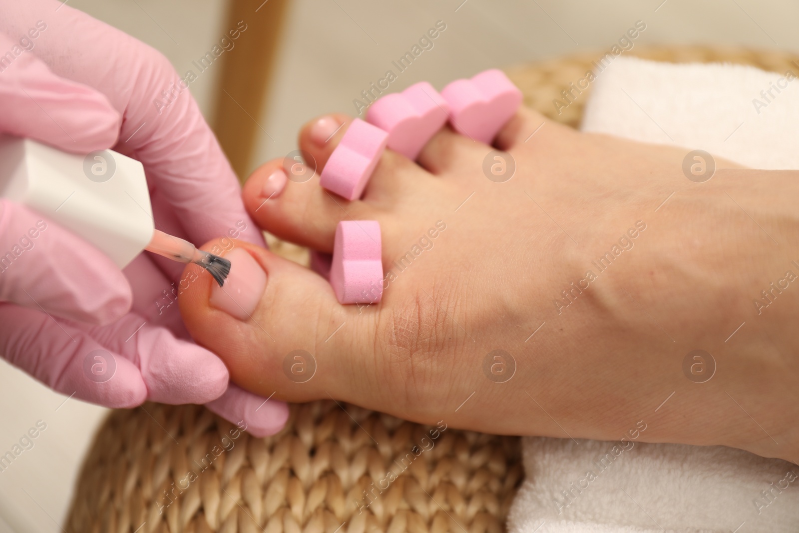 Photo of Professional pedicurist painting client`s toenails with polish in beauty salon, closeup