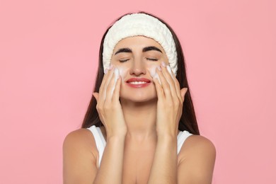 Photo of Beautiful woman applying cleansing foam onto face on pink background