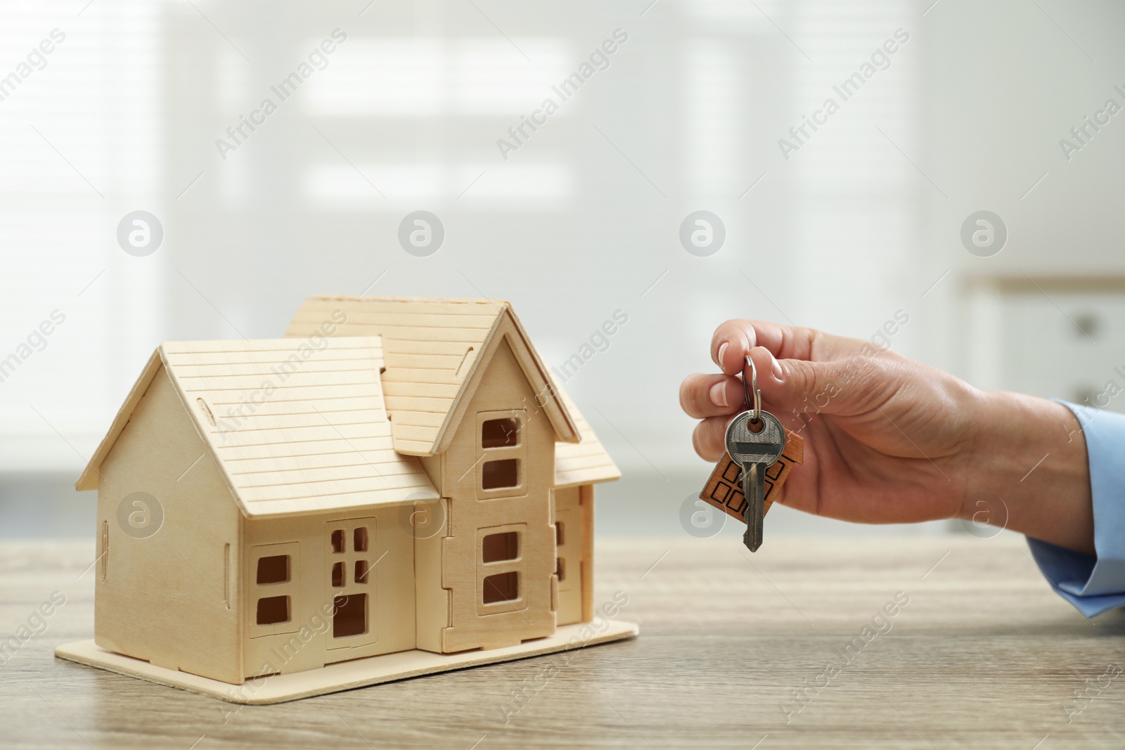 Photo of Real estate agent with house model and key at wooden table, closeup