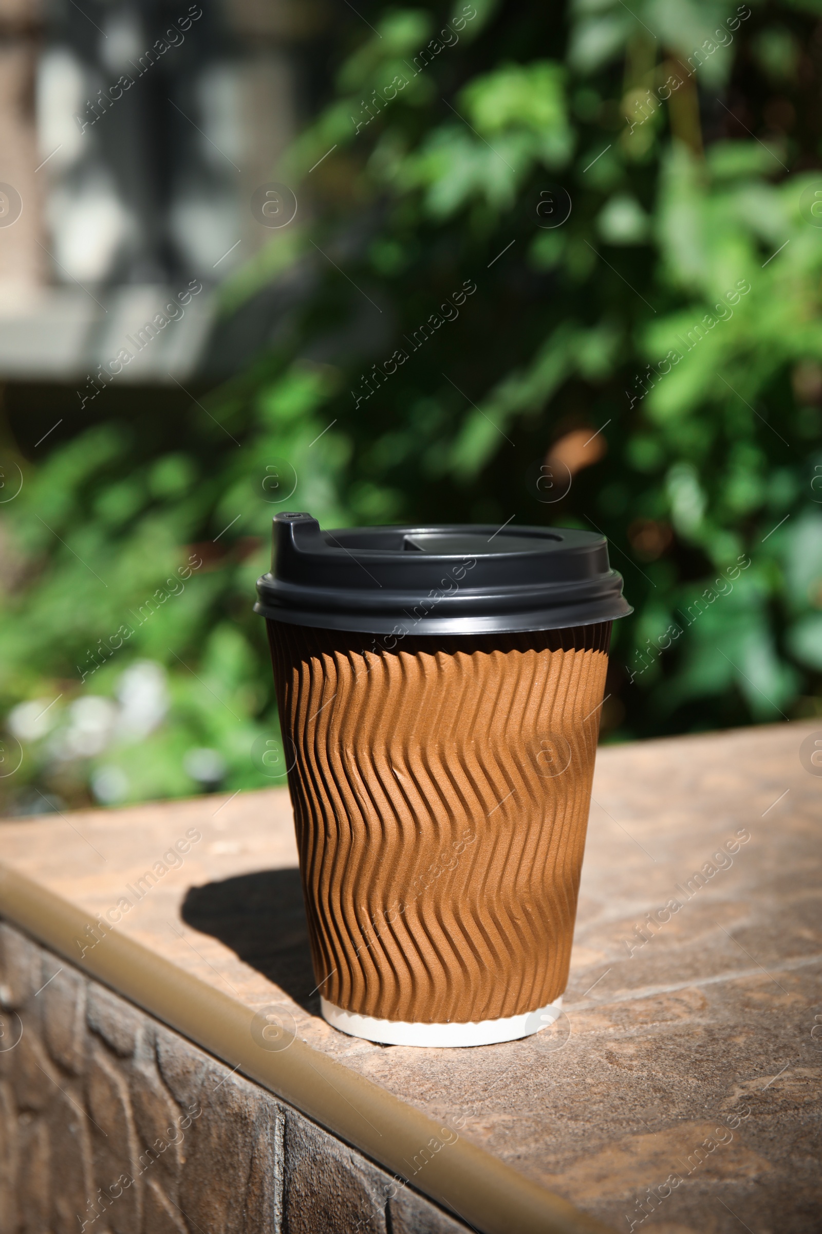 Photo of Takeaway cardboard coffee cup with plastic lid on stone surface outdoors