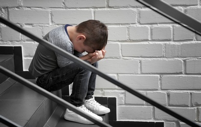 Photo of Sad little boy sitting on stairs indoors