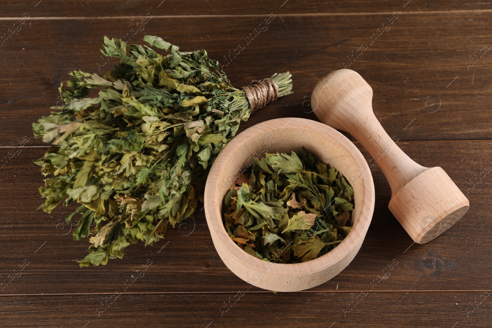 Photo of Mortar and pestle with dry parsley on wooden table, above view