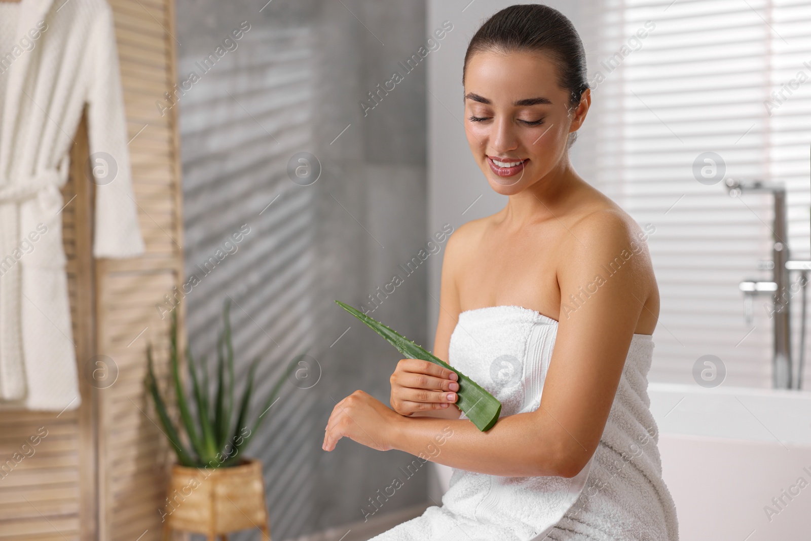 Photo of Young woman applying aloe gel onto her arm in bathroom. Space for text