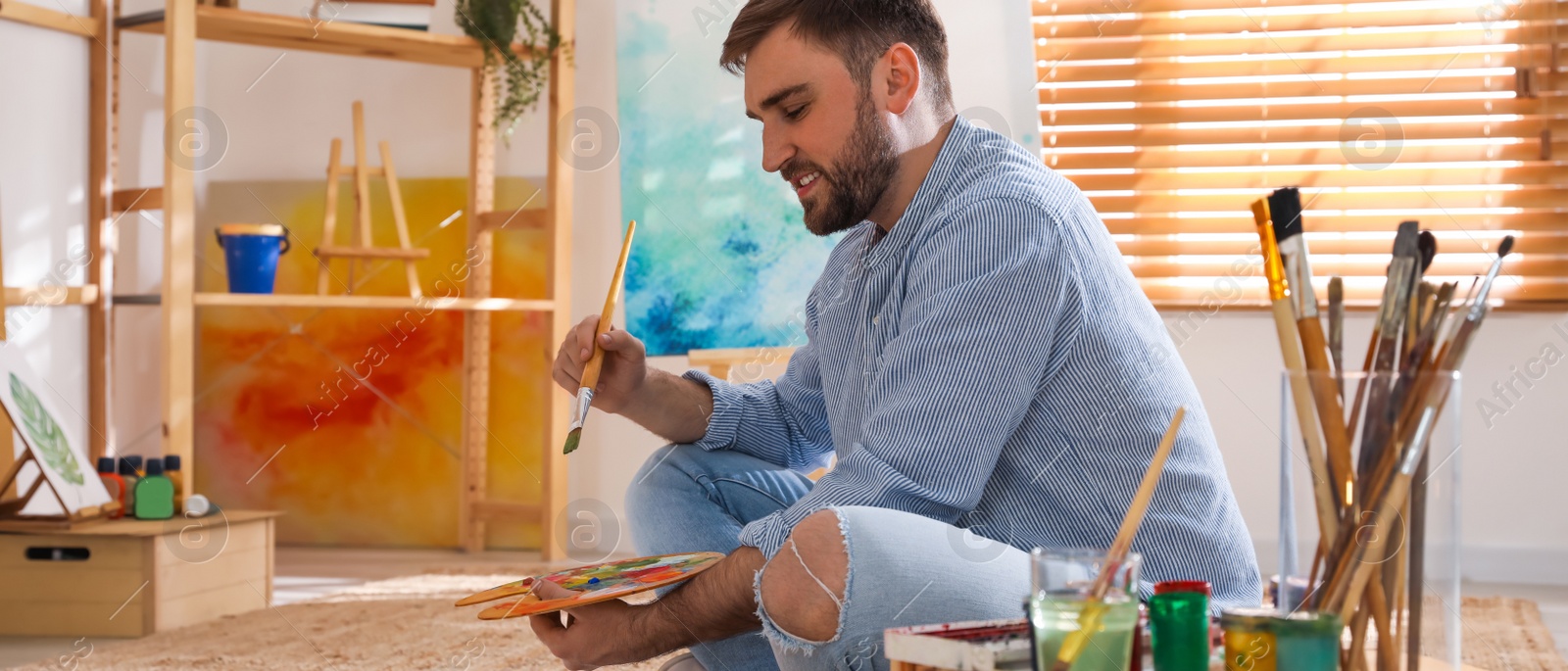 Image of Young man painting with brush in artist studio. Banner design