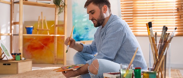 Young man painting with brush in artist studio. Banner design