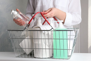 Woman with shopping basket full of antiseptics and toilet paper at table indoors, closeup. Panic caused by virus