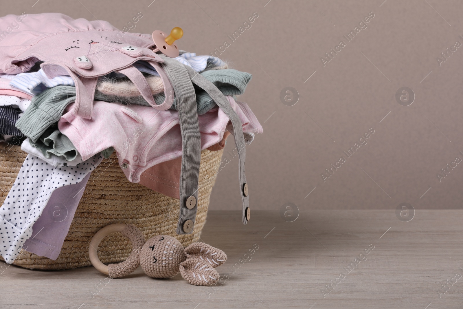 Photo of Laundry basket with baby clothes and soft toy on wooden table, space for text