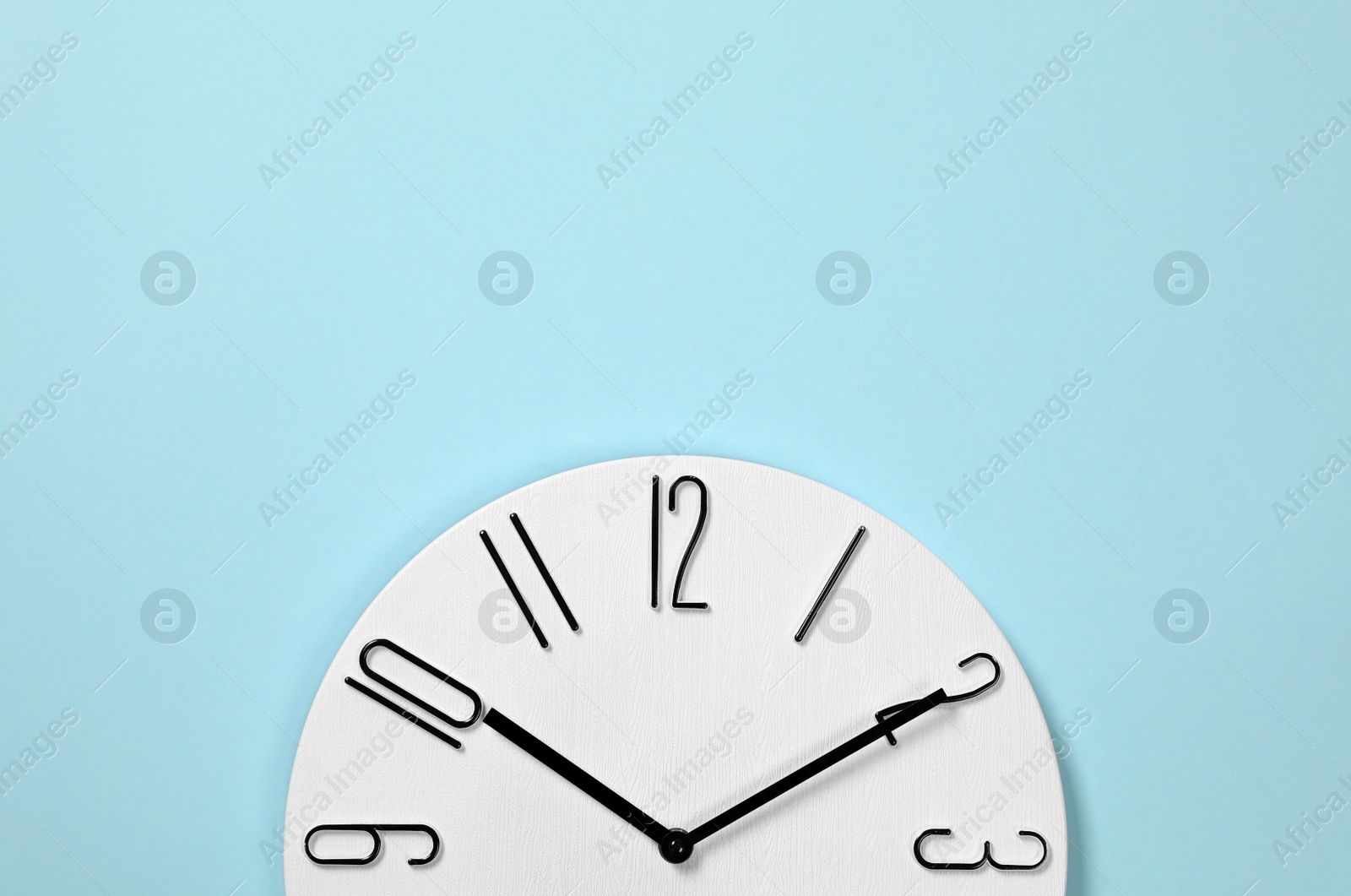 Photo of Stylish analog clock hanging on light blue wall, space for text