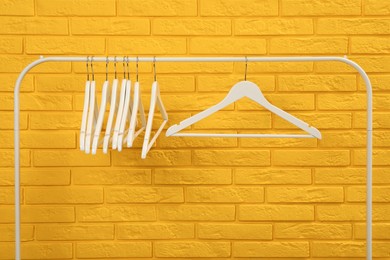 Photo of Wardrobe rack with many hangers near yellow brick wall
