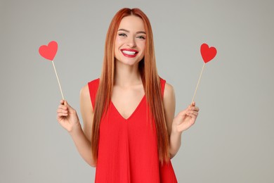 Photo of Young woman in red dress with paper hearts on light grey background