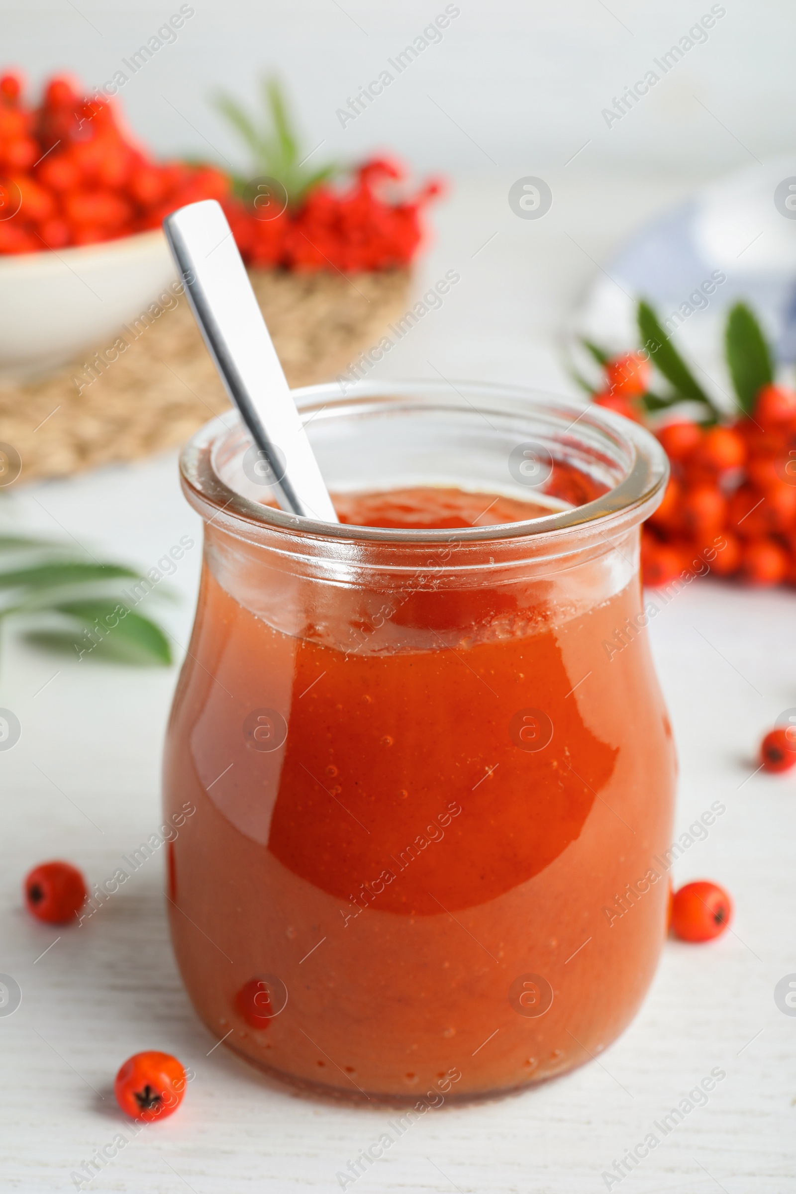 Photo of Delicious rowan jam in glass jar on white wooden table