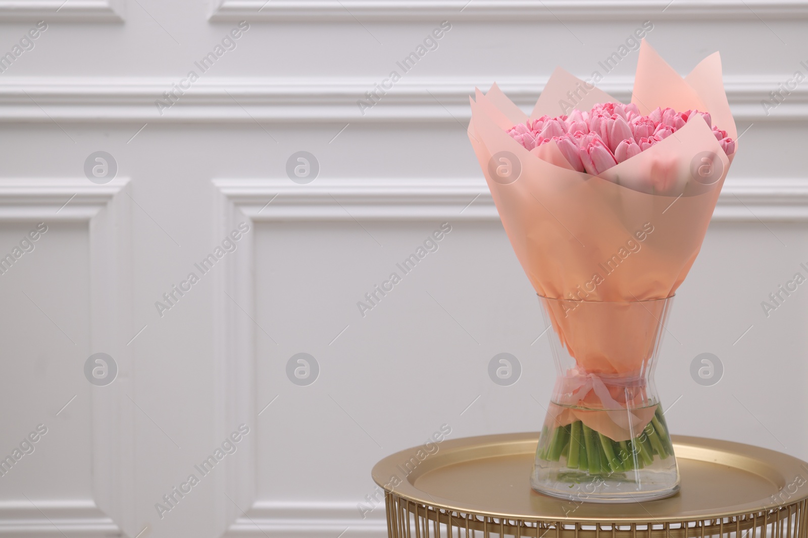 Photo of Bouquet of beautiful pink tulips in vase on table near white wall, space for text