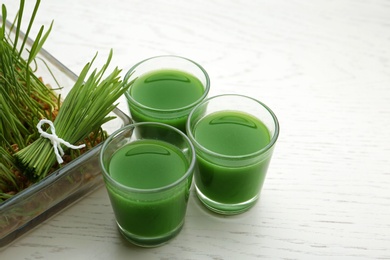Photo of Glasses of wheat grass juice and sprouts on white wooden background