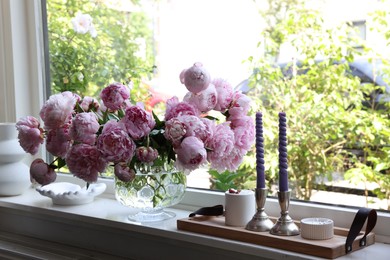 Photo of Beautiful pink peonies in vase and tray with candles on window sill. Interior design